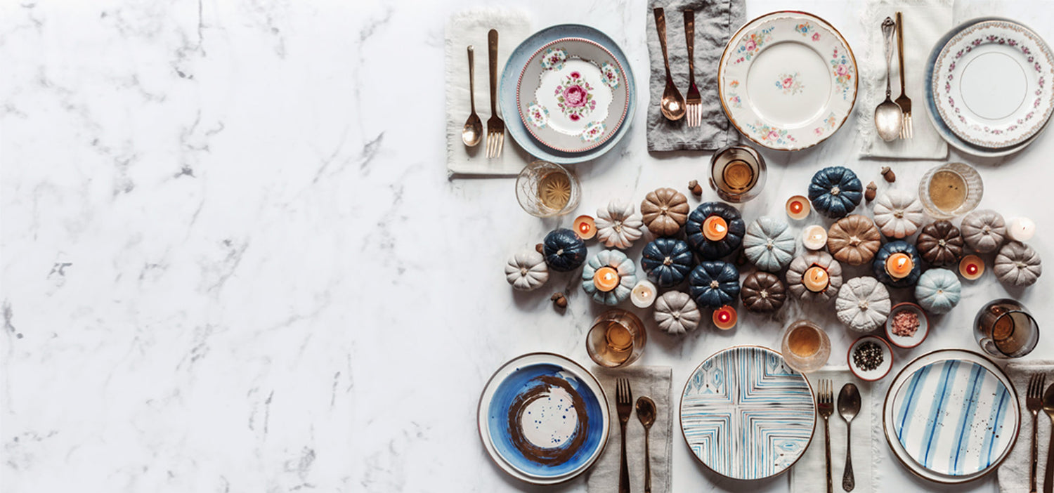 Six assiettes vintage avec des ustensiles dorés avec serviette de table en lin pâle plusieurs petites citrouilles colorée et chandelles sur comptoir de marbre blanc et gris